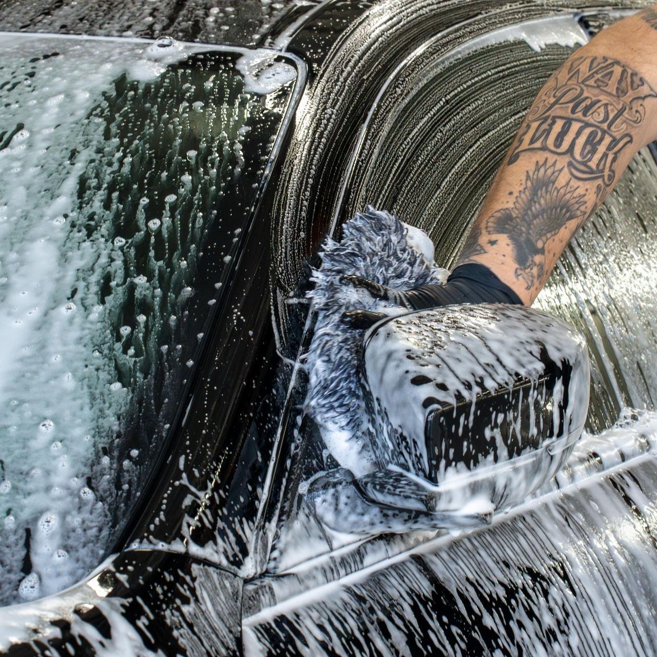 A man with a tattoo on his arm is washing a car