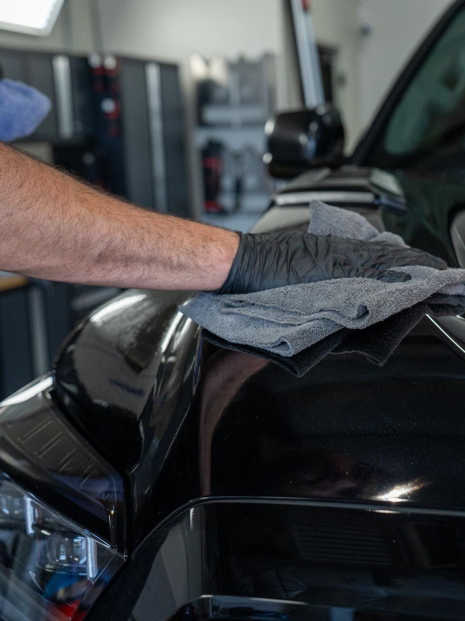 A man is cleaning the hood of a black car with a towel.