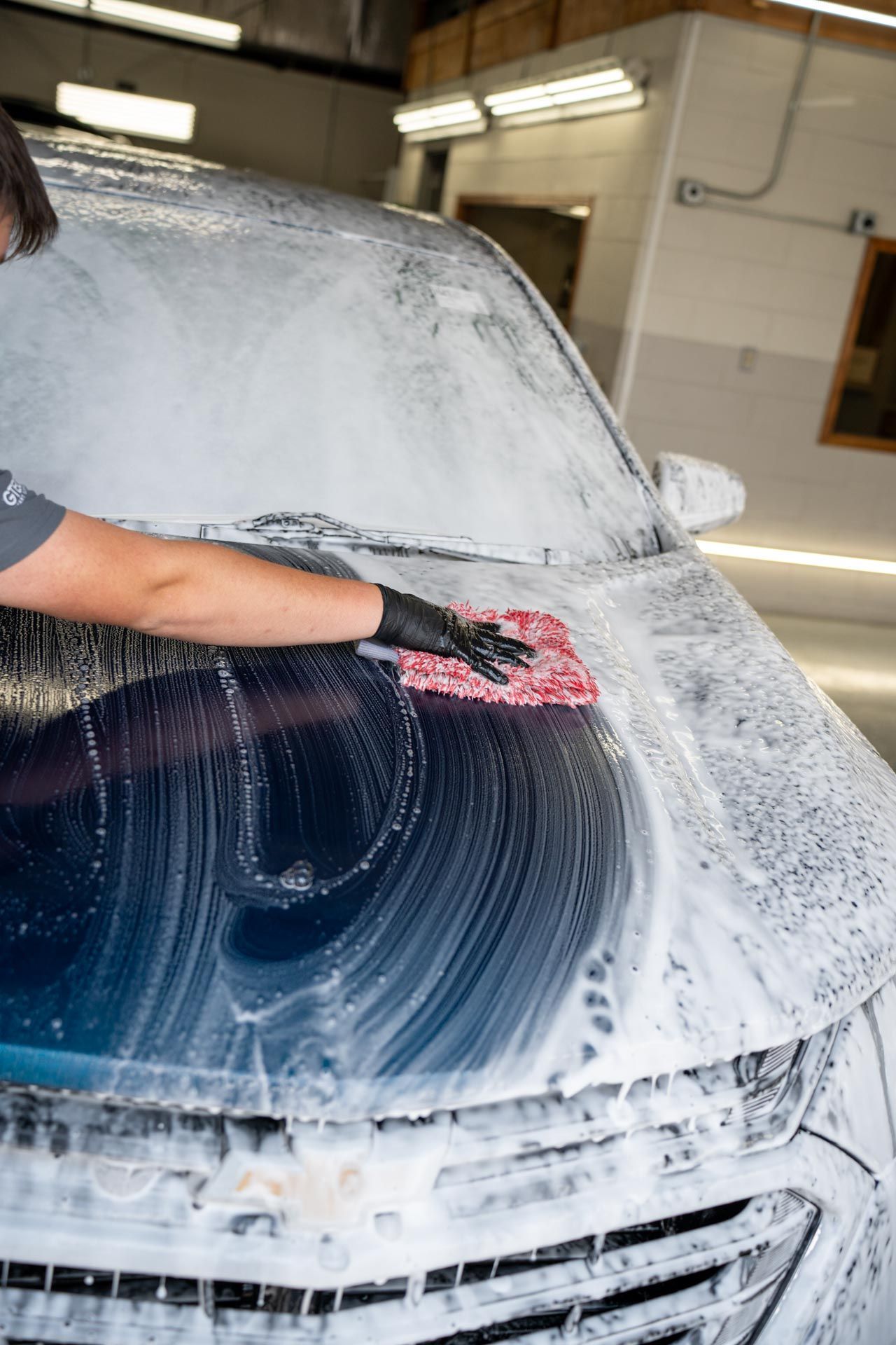 A person wearing black gloves is cleaning a white car with a cloth