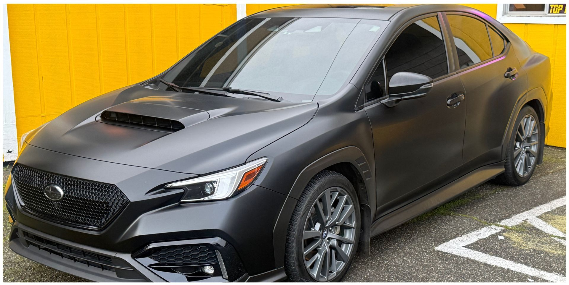 Black Subaru WRX sedan parked in front of a yellow wall.