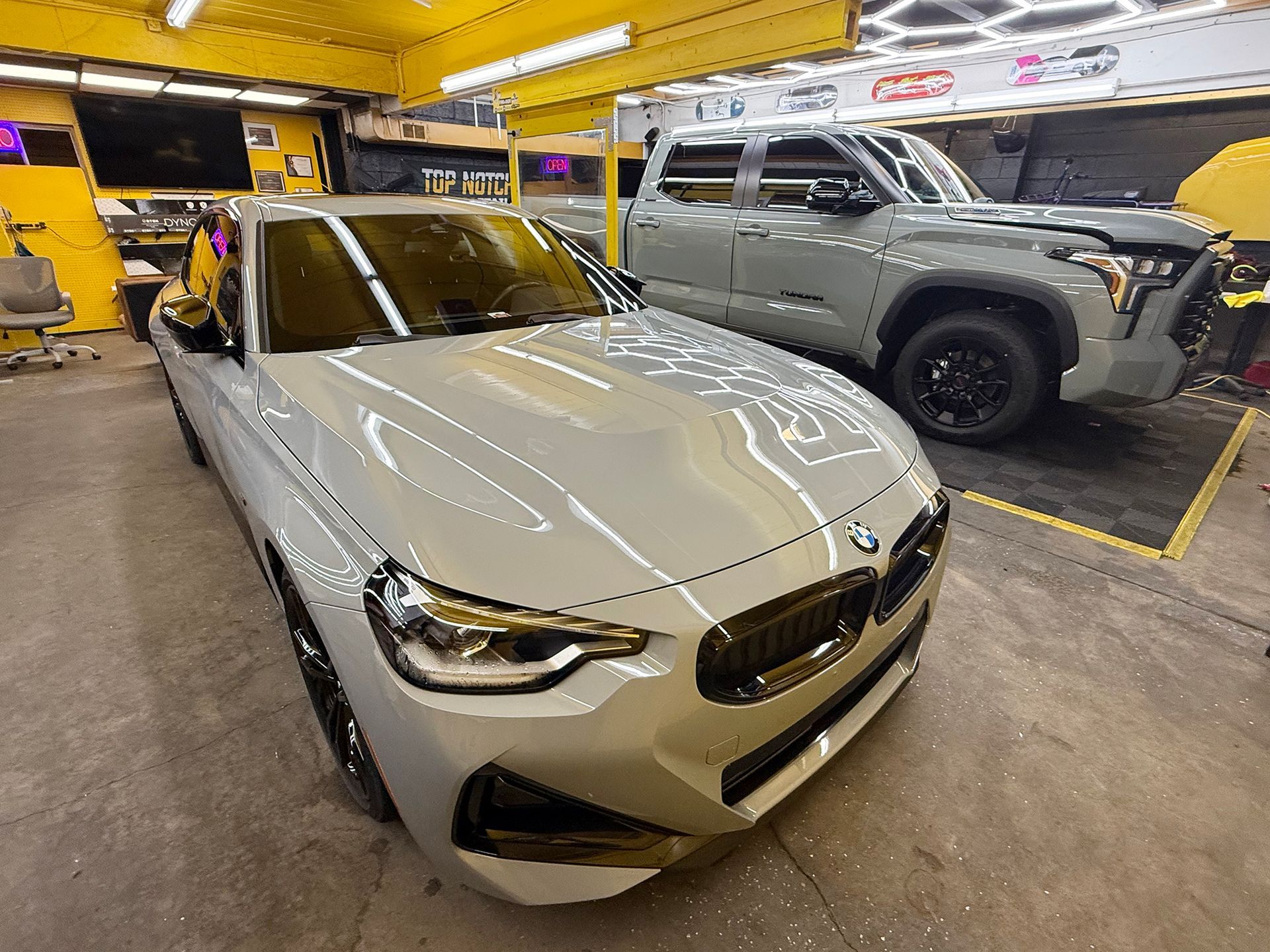 A white car is parked next to a silver truck in a garage.