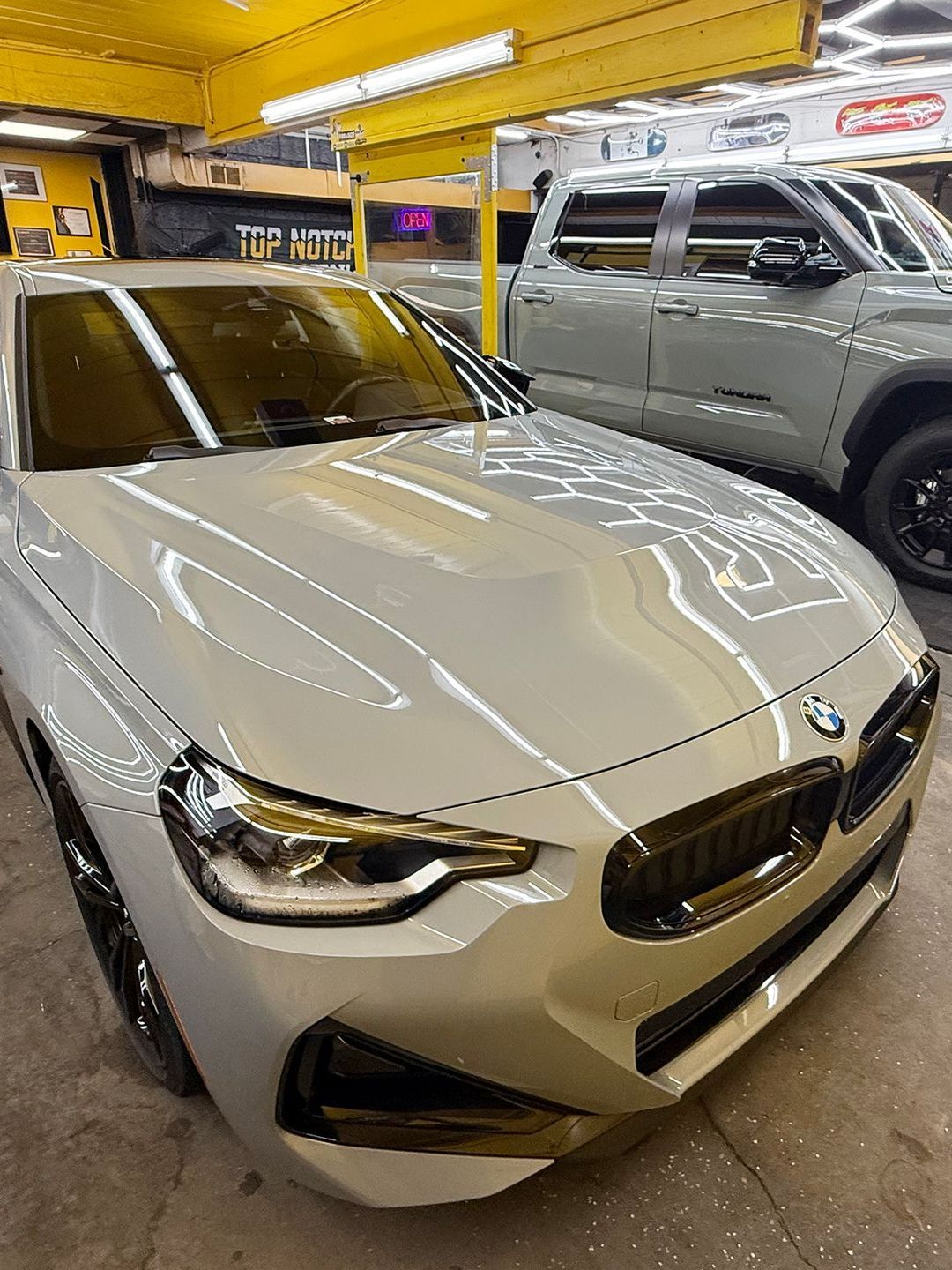 A white bmw is parked next to a silver truck in a garage.