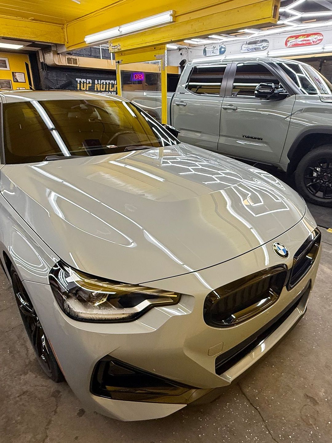 A white bmw is parked in a garage next to a truck.