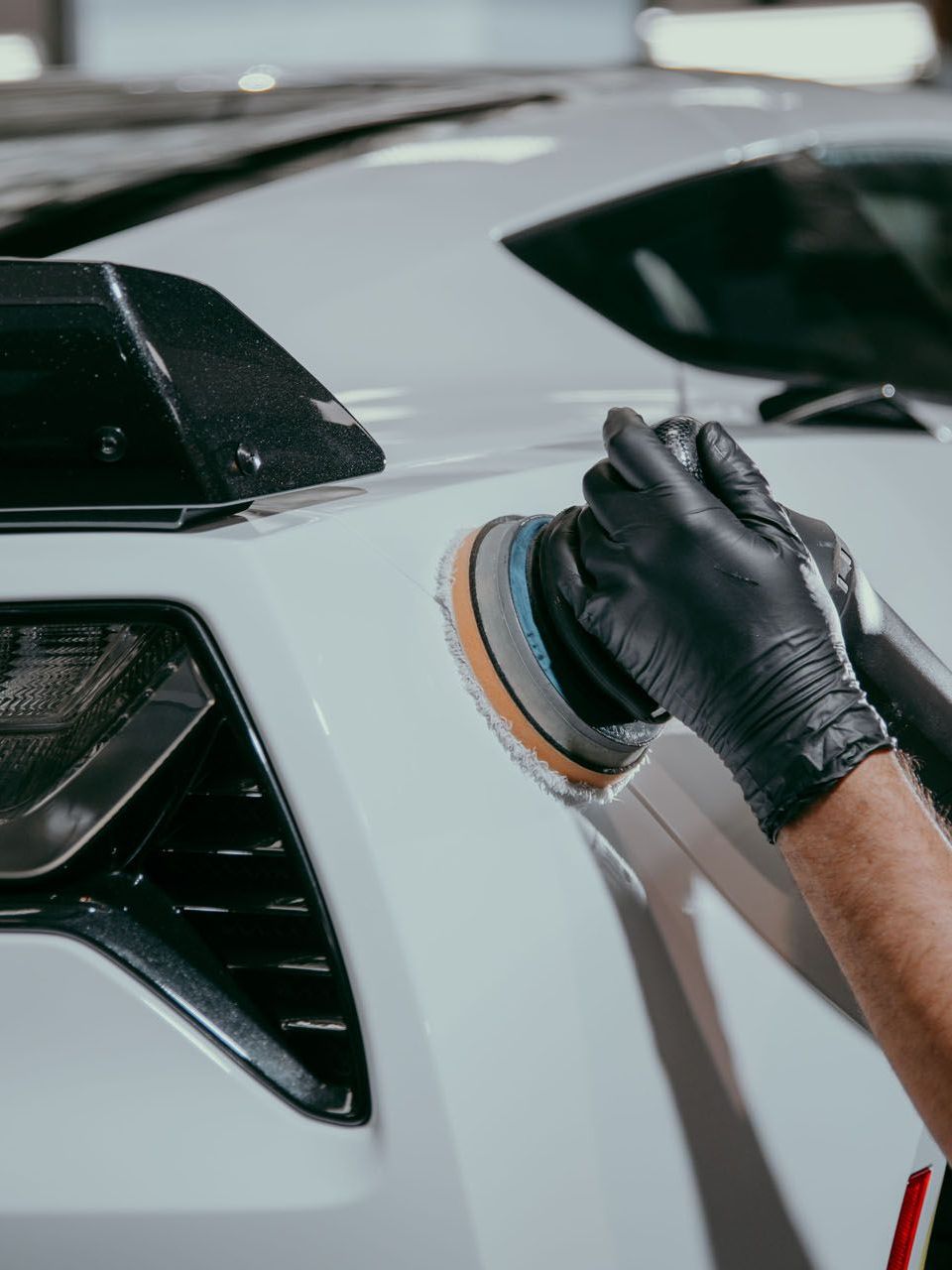 A person wearing black gloves is polishing a white car.