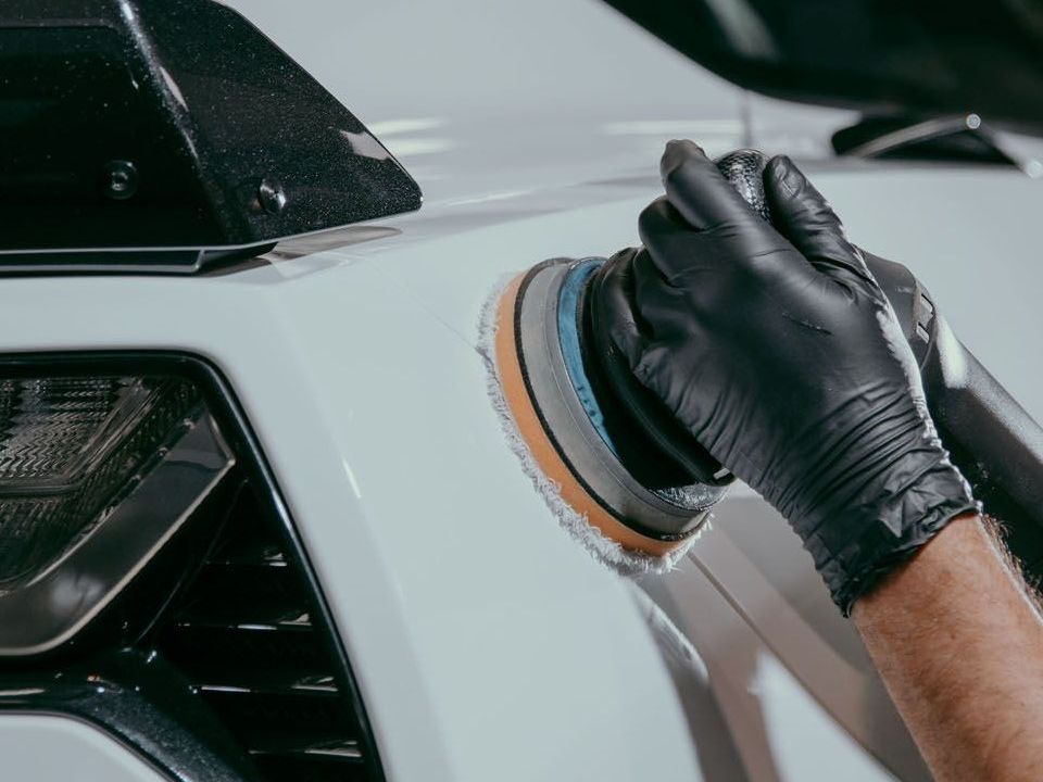 A person wearing black gloves is polishing a white car.