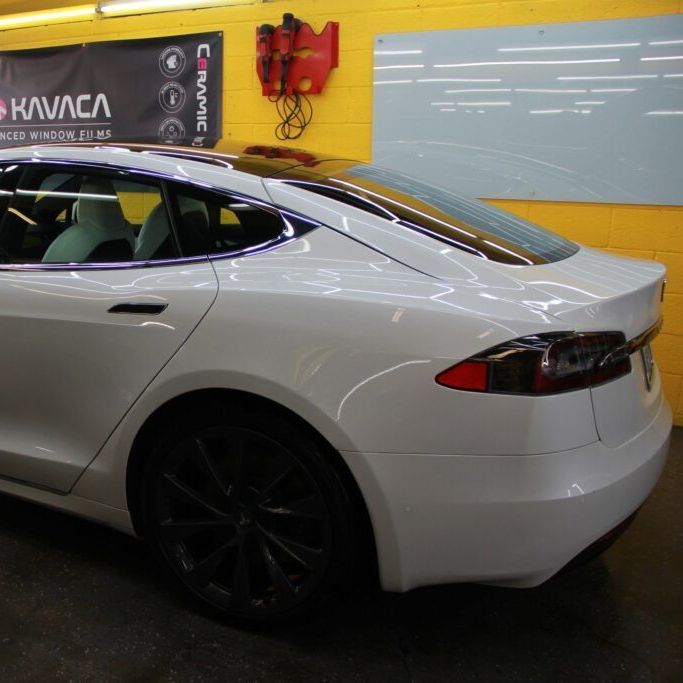 A white car is parked in front of a sign that says kavaca