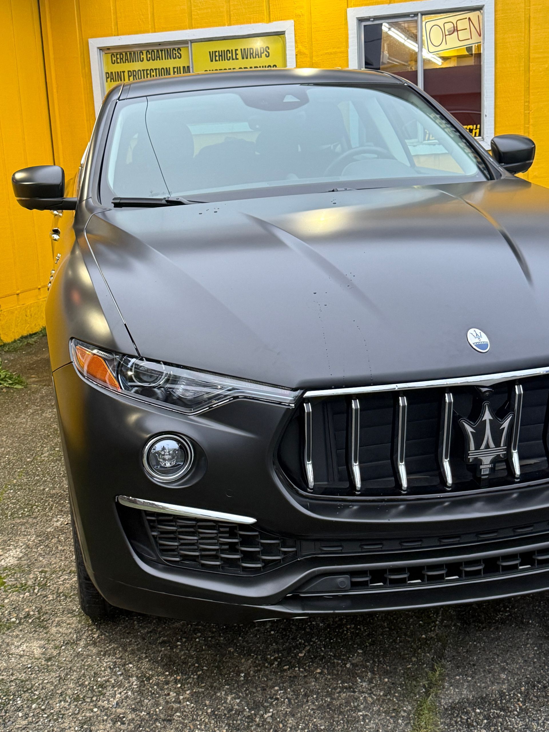 A dark gray Maserati SUV parked in front of a yellow building.