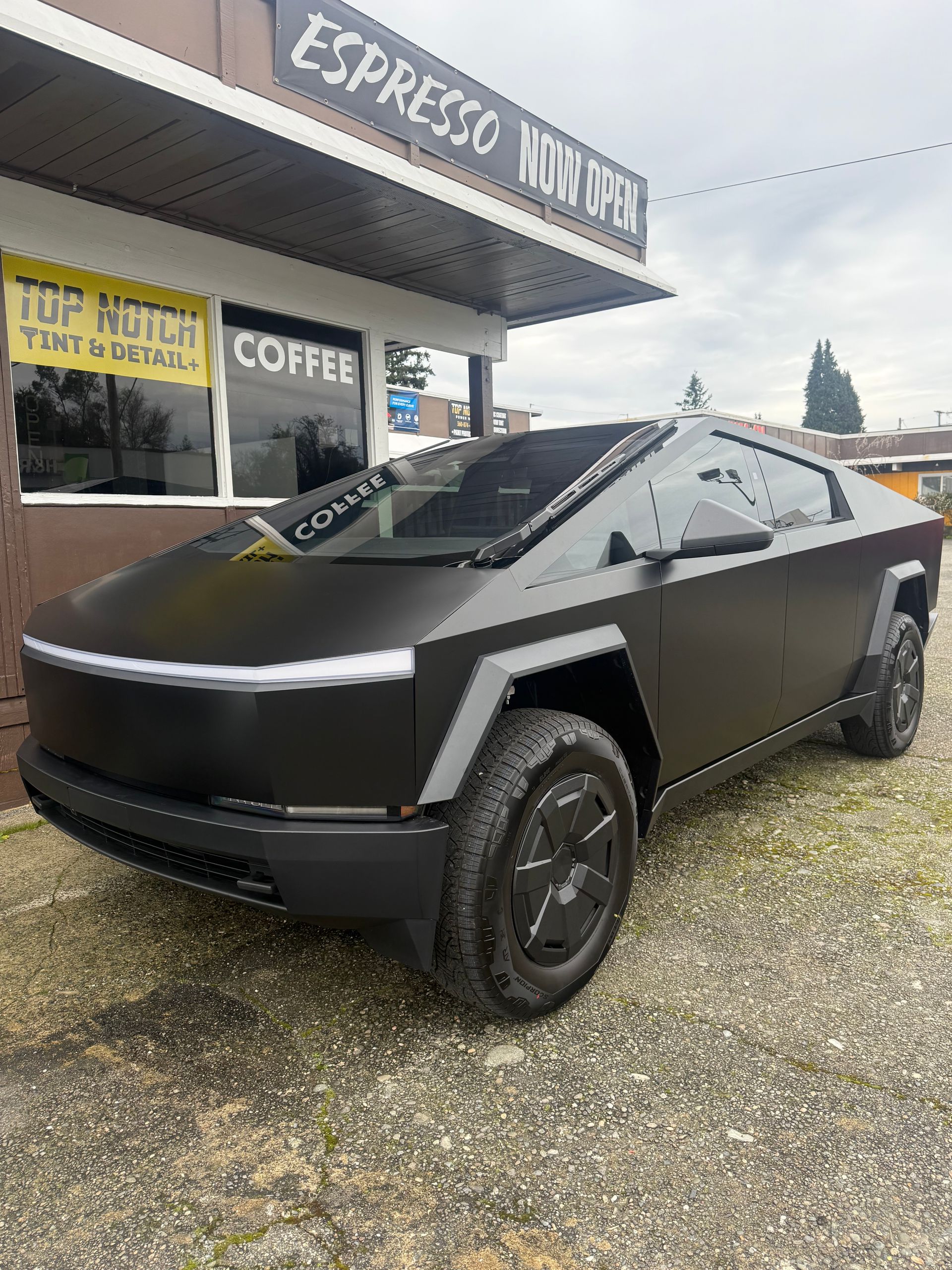 Black Tesla Cybertruck parked outside a coffee shop with a 