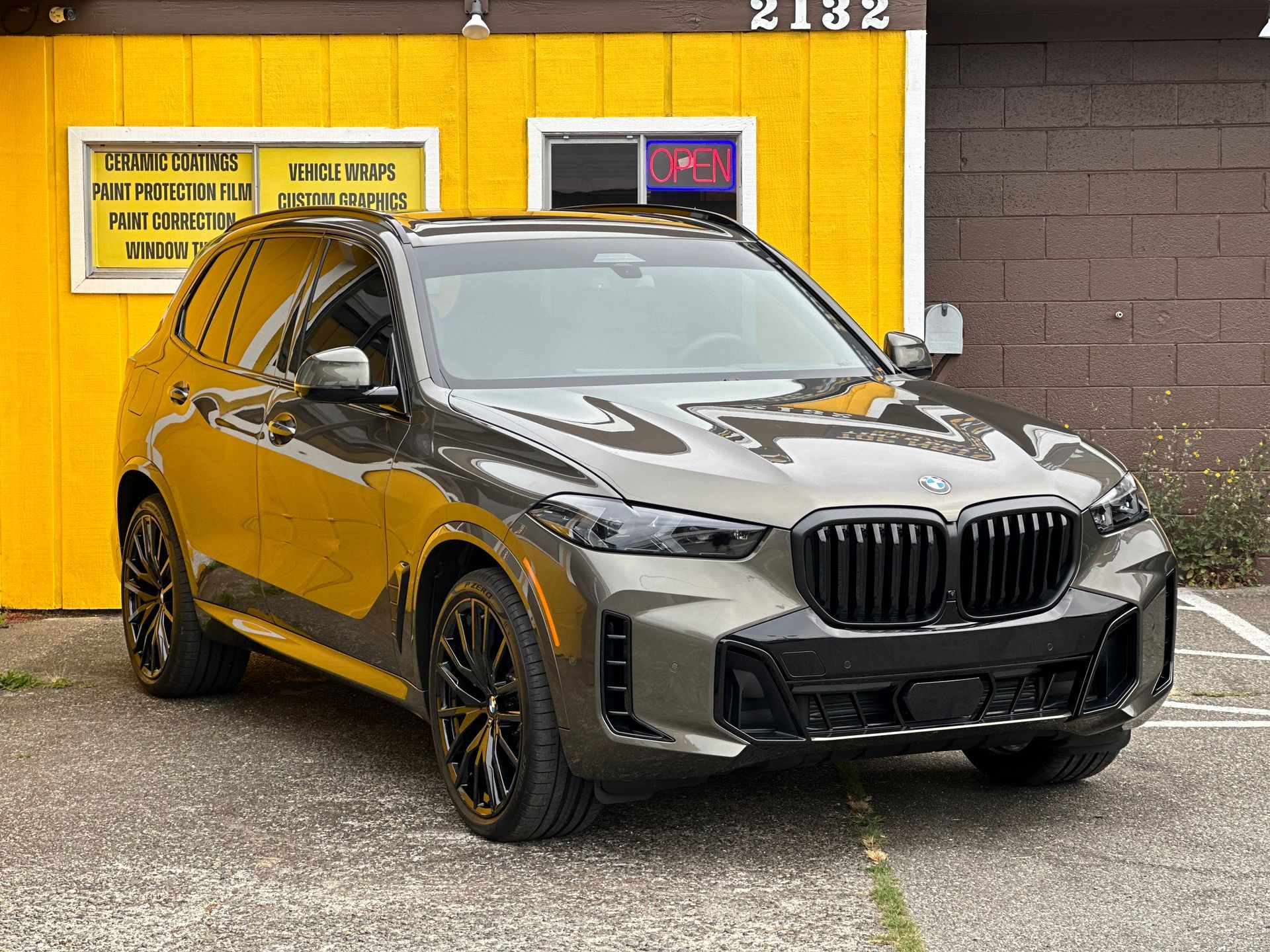 A bmw x5 is parked in front of the Top Notch Tint & Detail building.