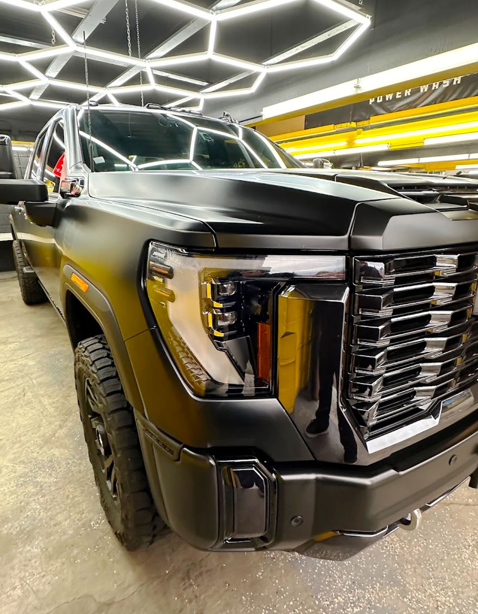 A black truck with a yellow grille is parked in a garage.