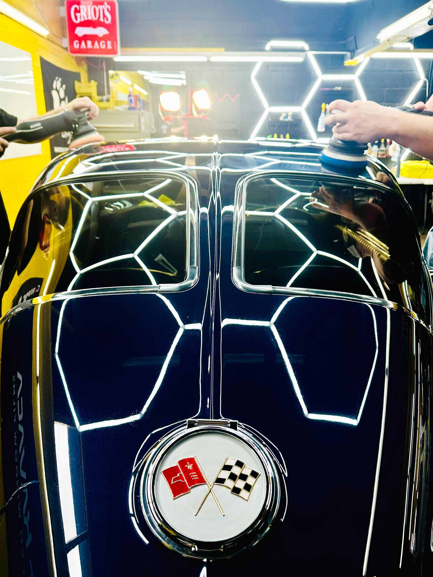 A man is polishing the hood of a corvette in a garage.