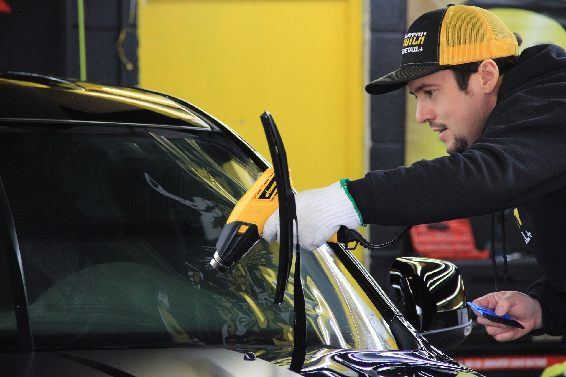A person wearing black gloves is polishing the hood of a red car.