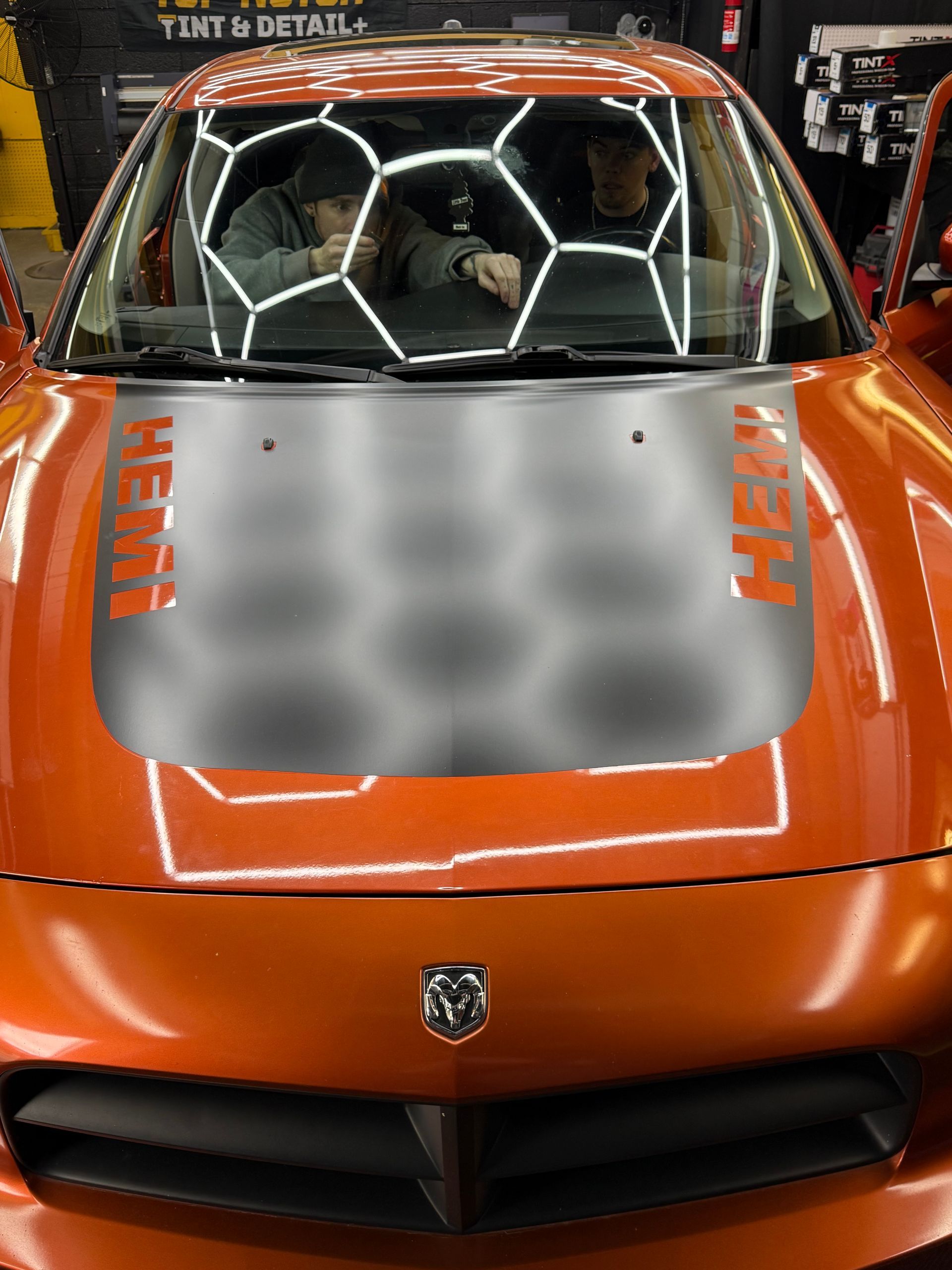 Orange Dodge Charger with a Hemi decal on hood; two people inside, likely working.
