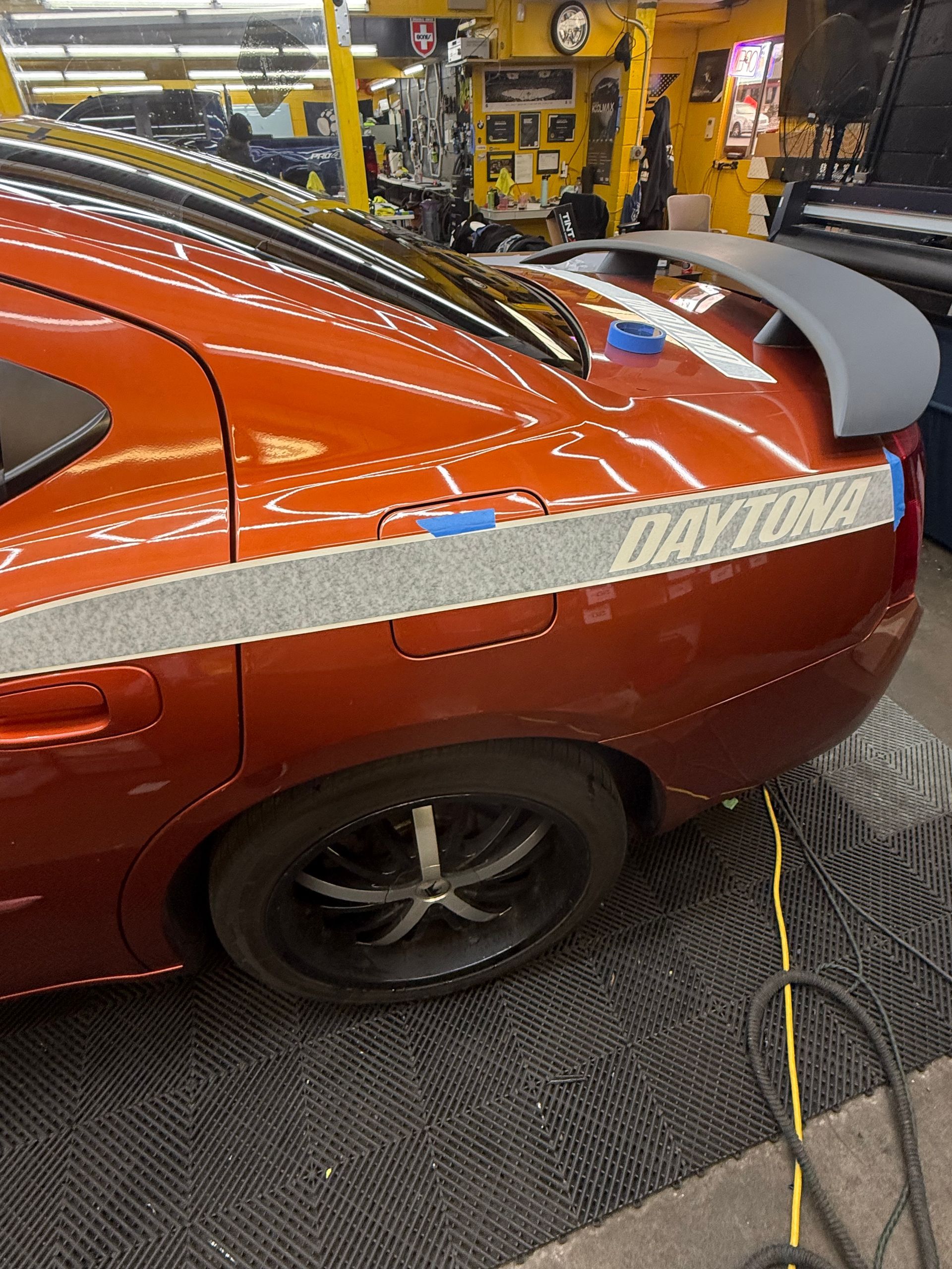 Orange Dodge Charger with Daytona stripe and spoiler, inside a shop.