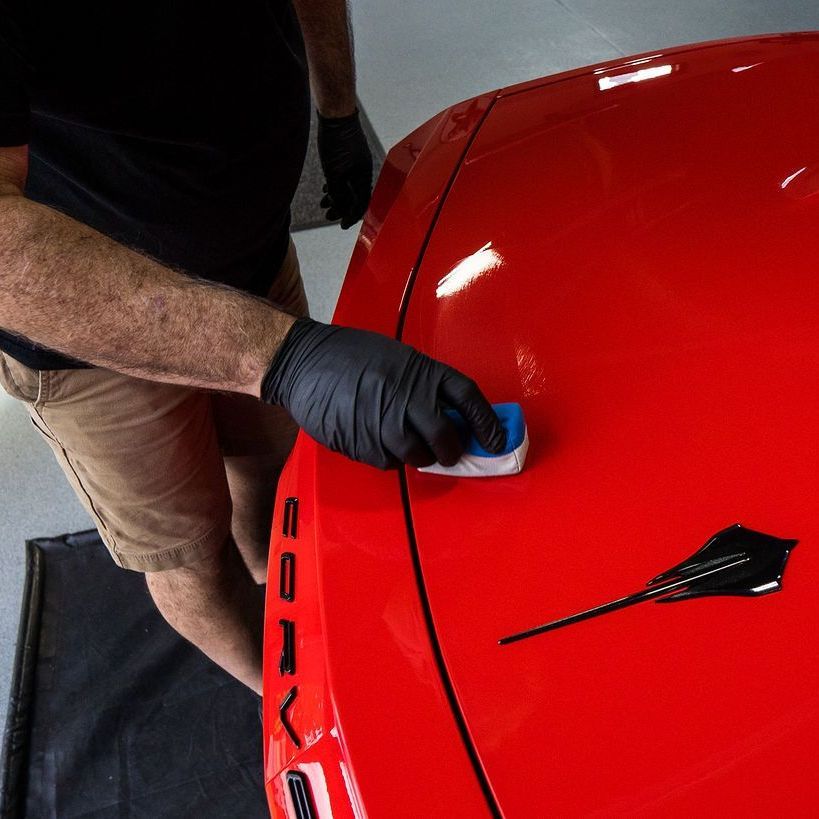 A person is cleaning a blue car with an orange towel