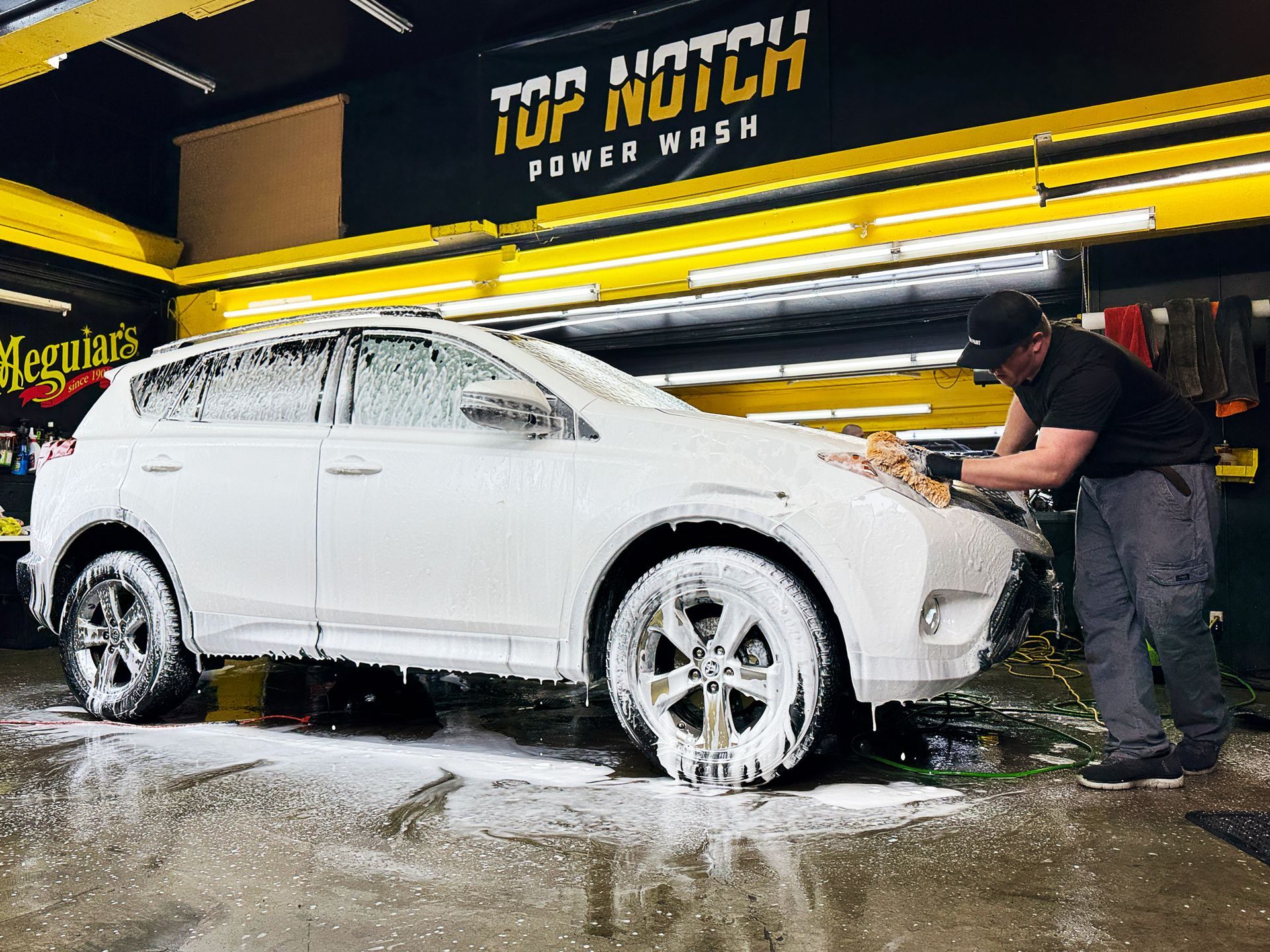 A man is washing a white suv in a car wash.