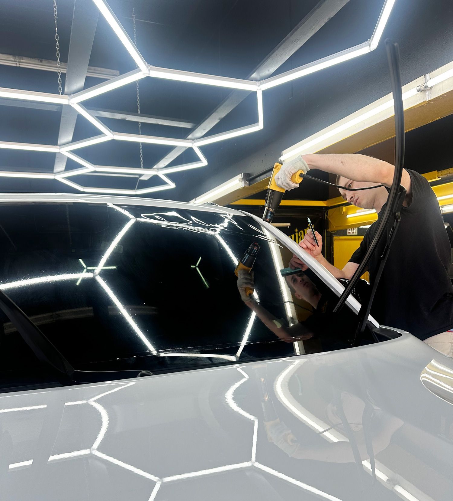 A person is polishing a white car with a machine.