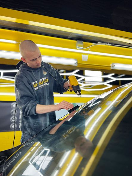A man is cleaning the windshield of a car in a garage.