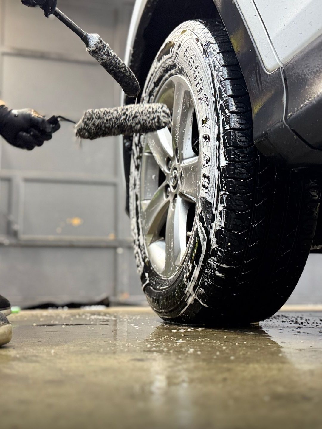 A person is cleaning a car wheel with a brush.