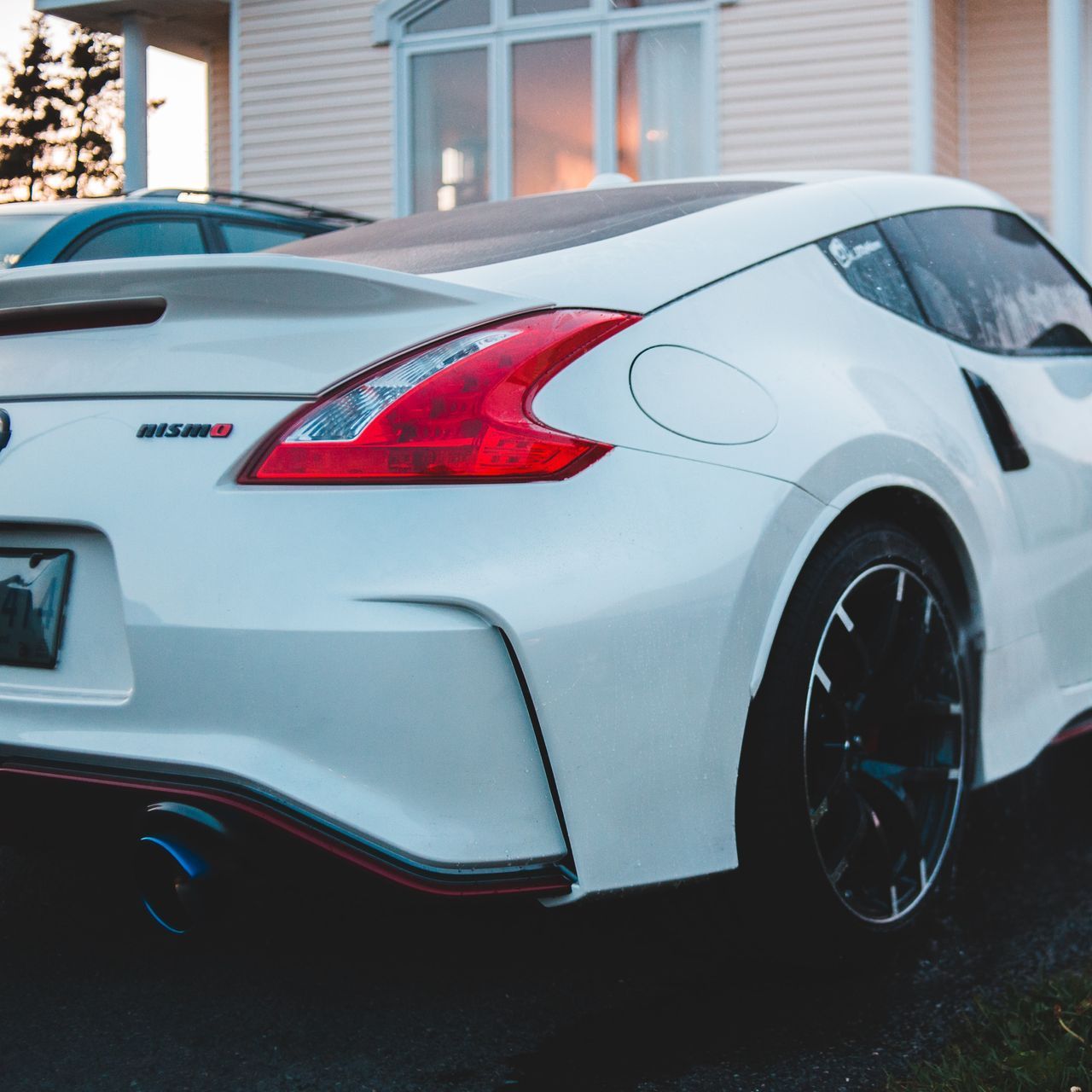 A white sports car with a red tail light is parked in front of a house