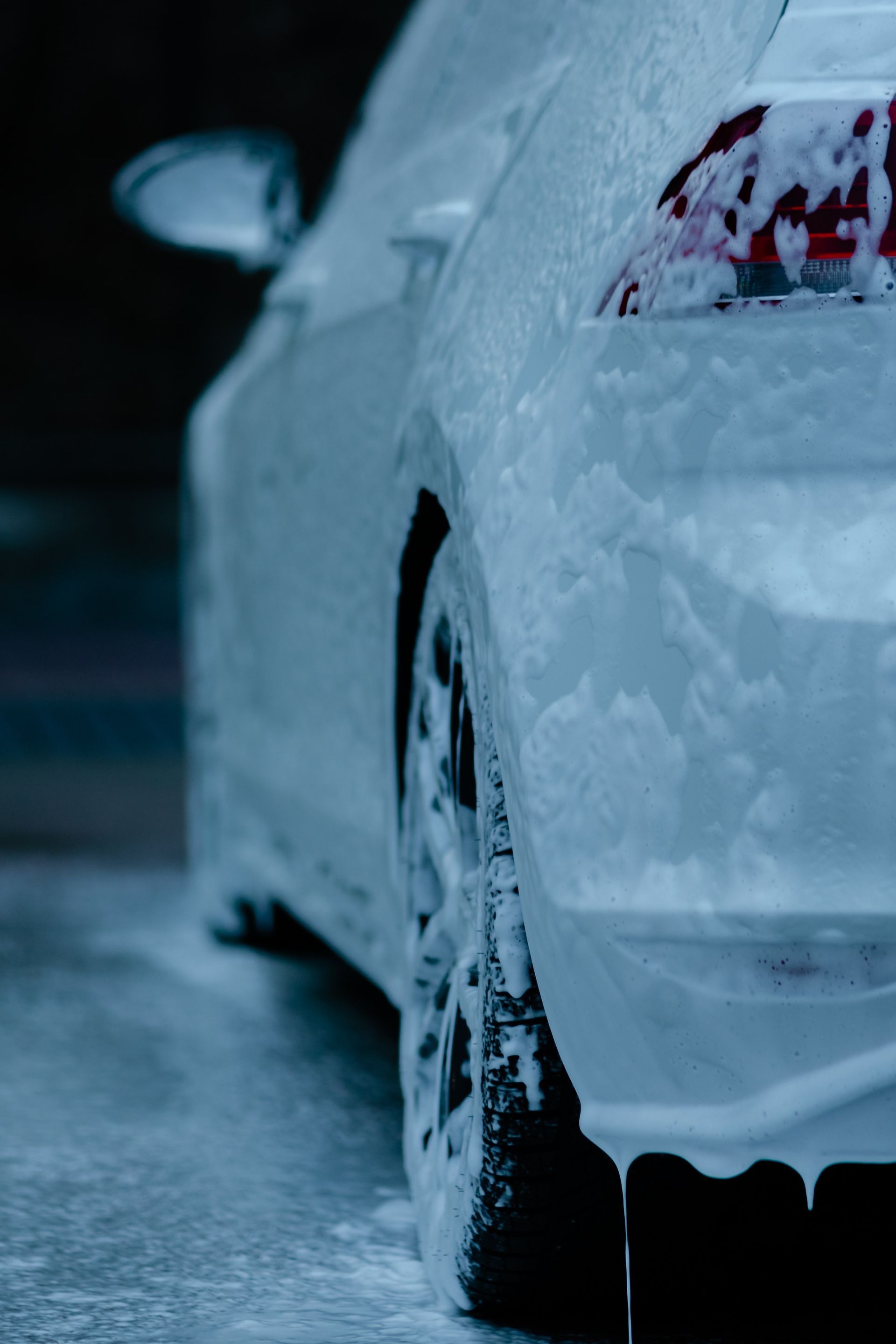A white car is covered in foam at a car wash.