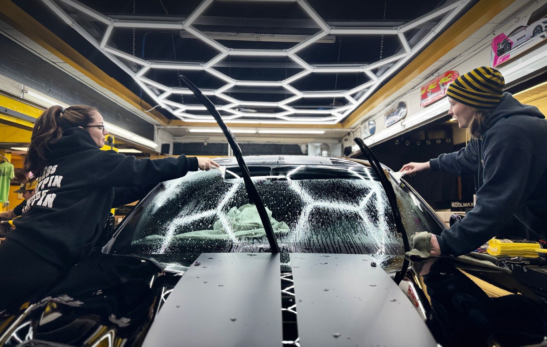 Two people are prepping the windshield of a car for window tint