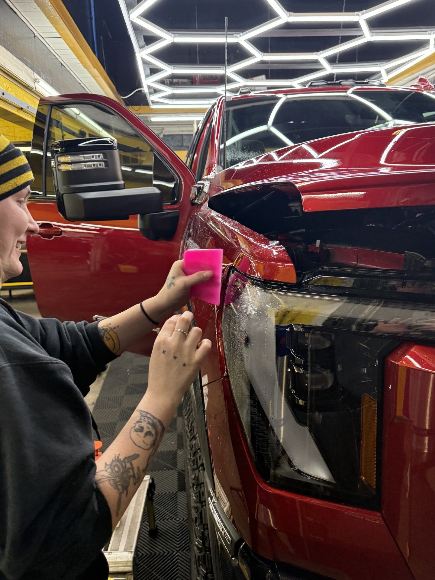 A person is applying a protective film to the front of a red truck.