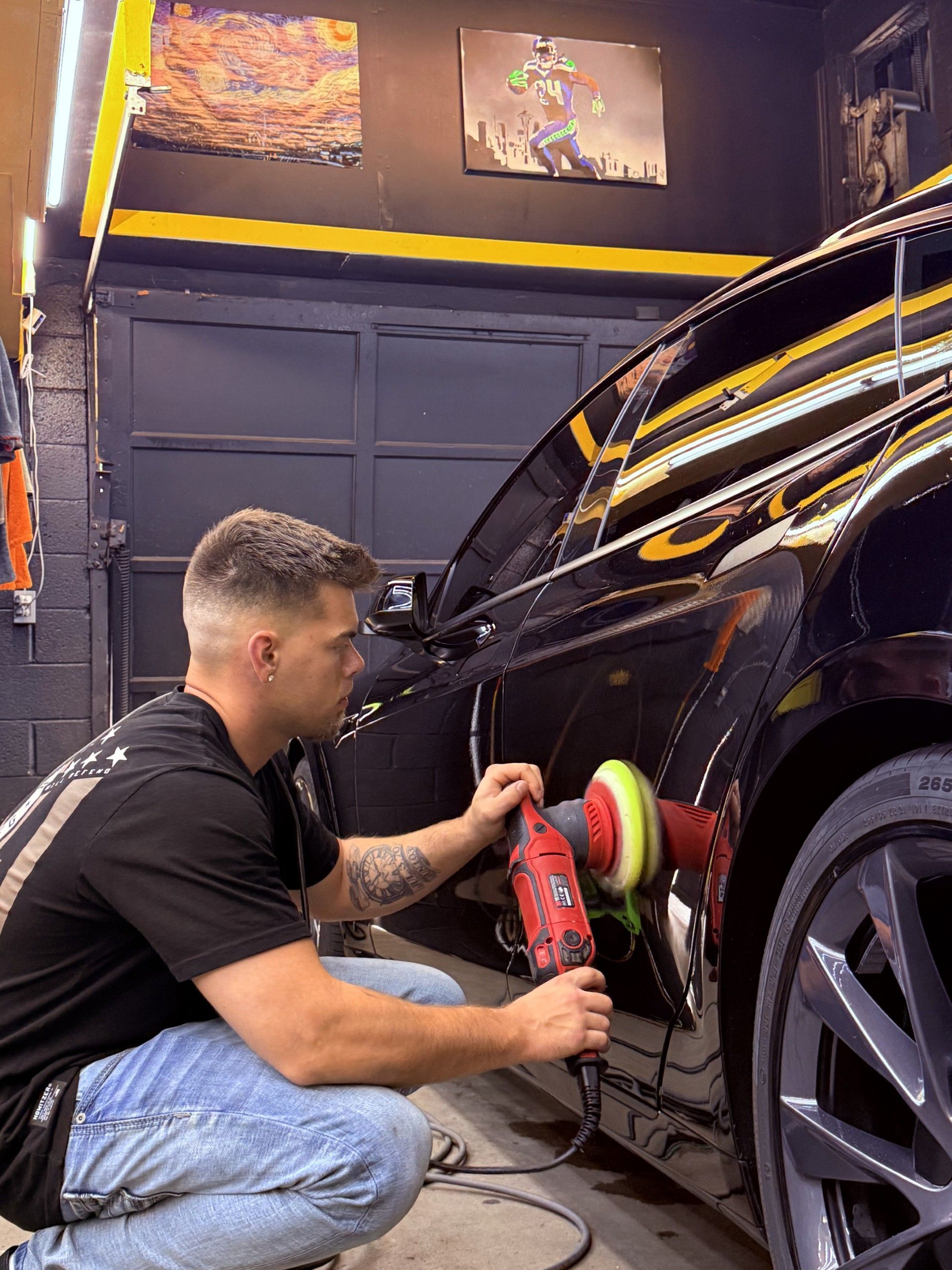 A man is polishing a black car with a machine.