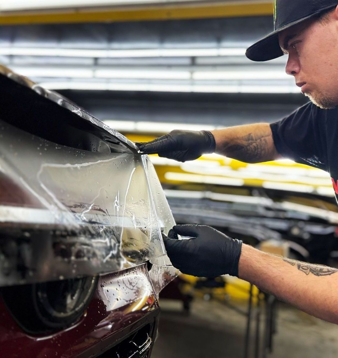 A man is applying a protective film to the front of a car.