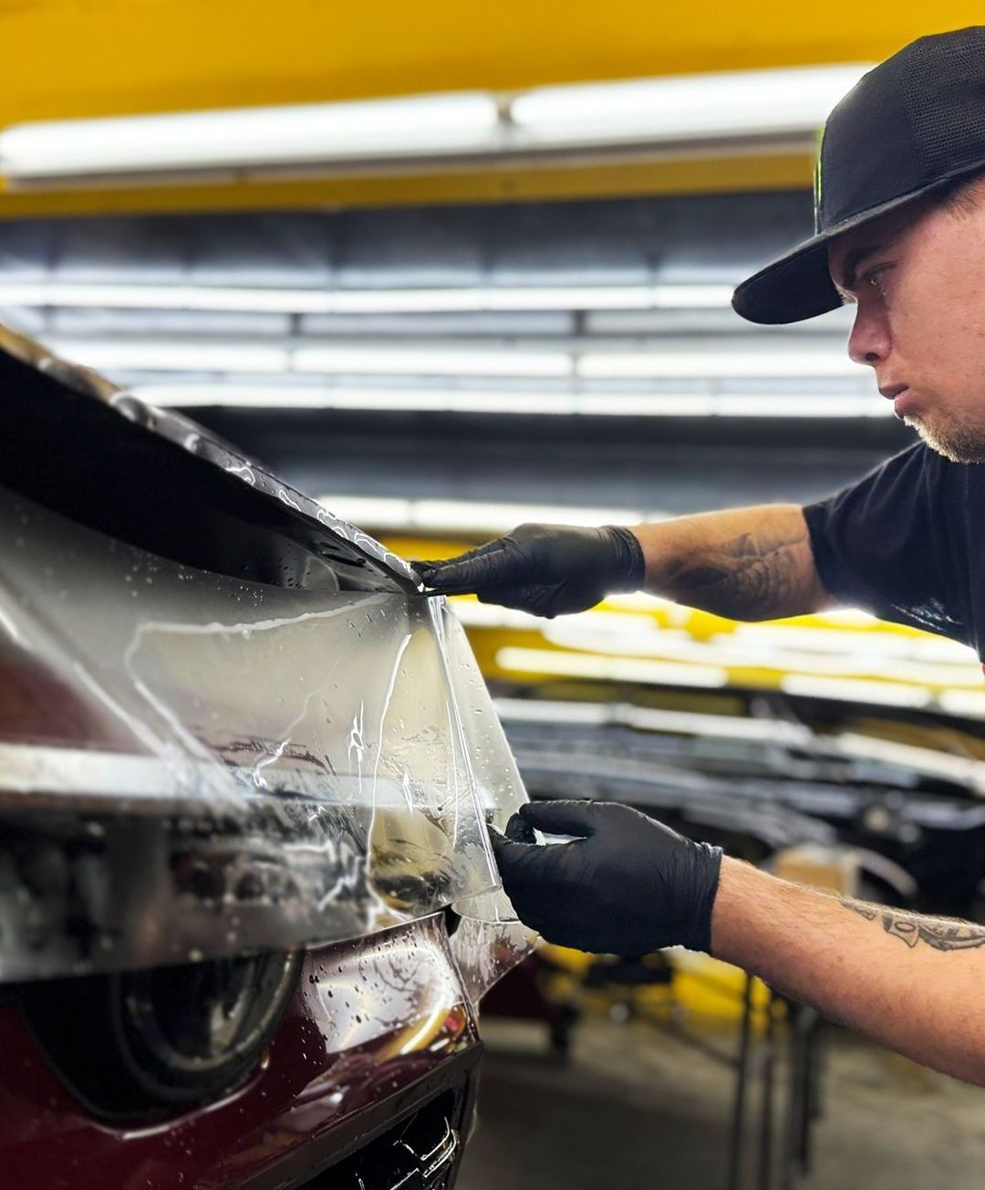 A man is wrapping a car with a plastic sheet.