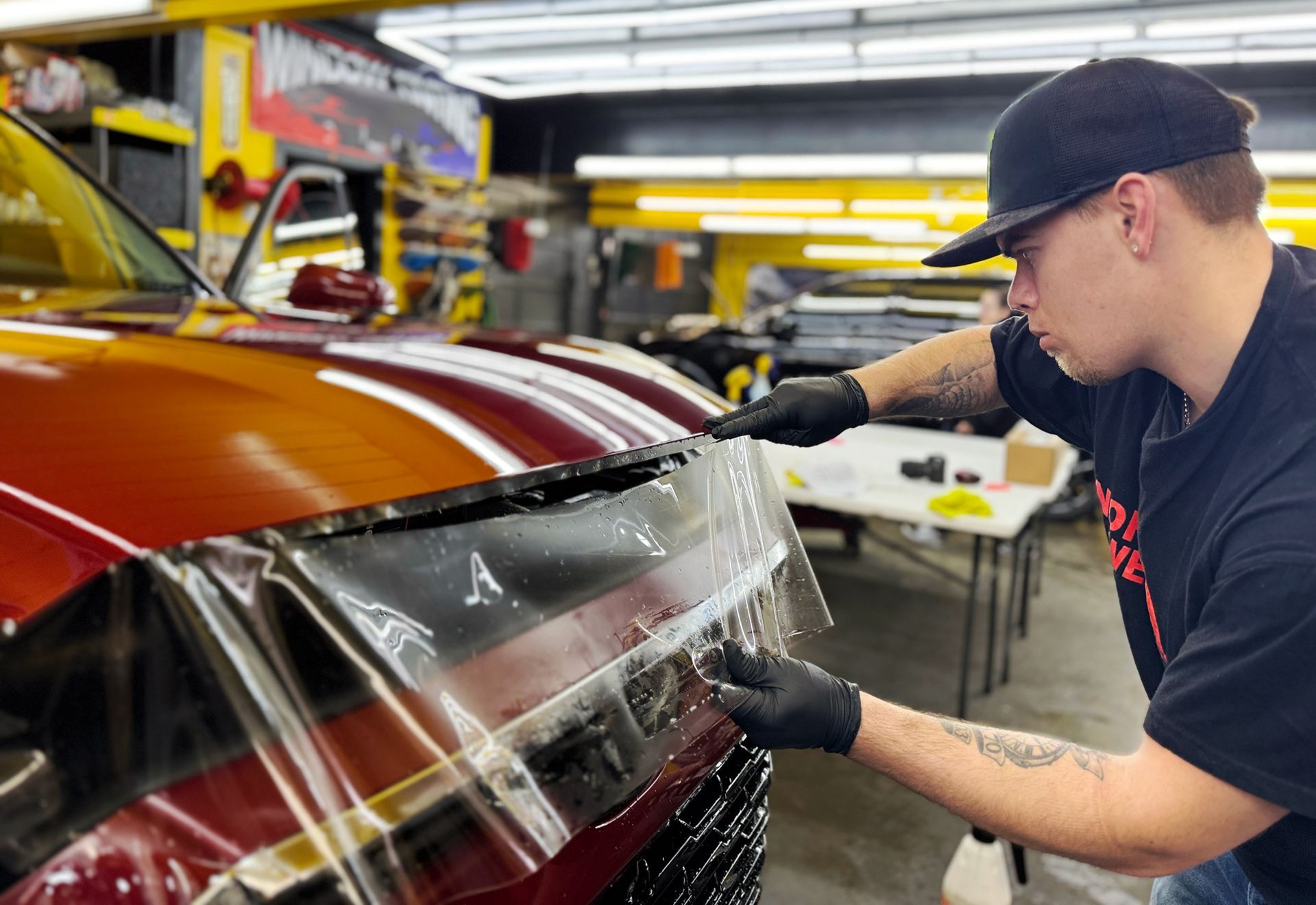 A man is wrapping the hood of a red truck with a clear film.