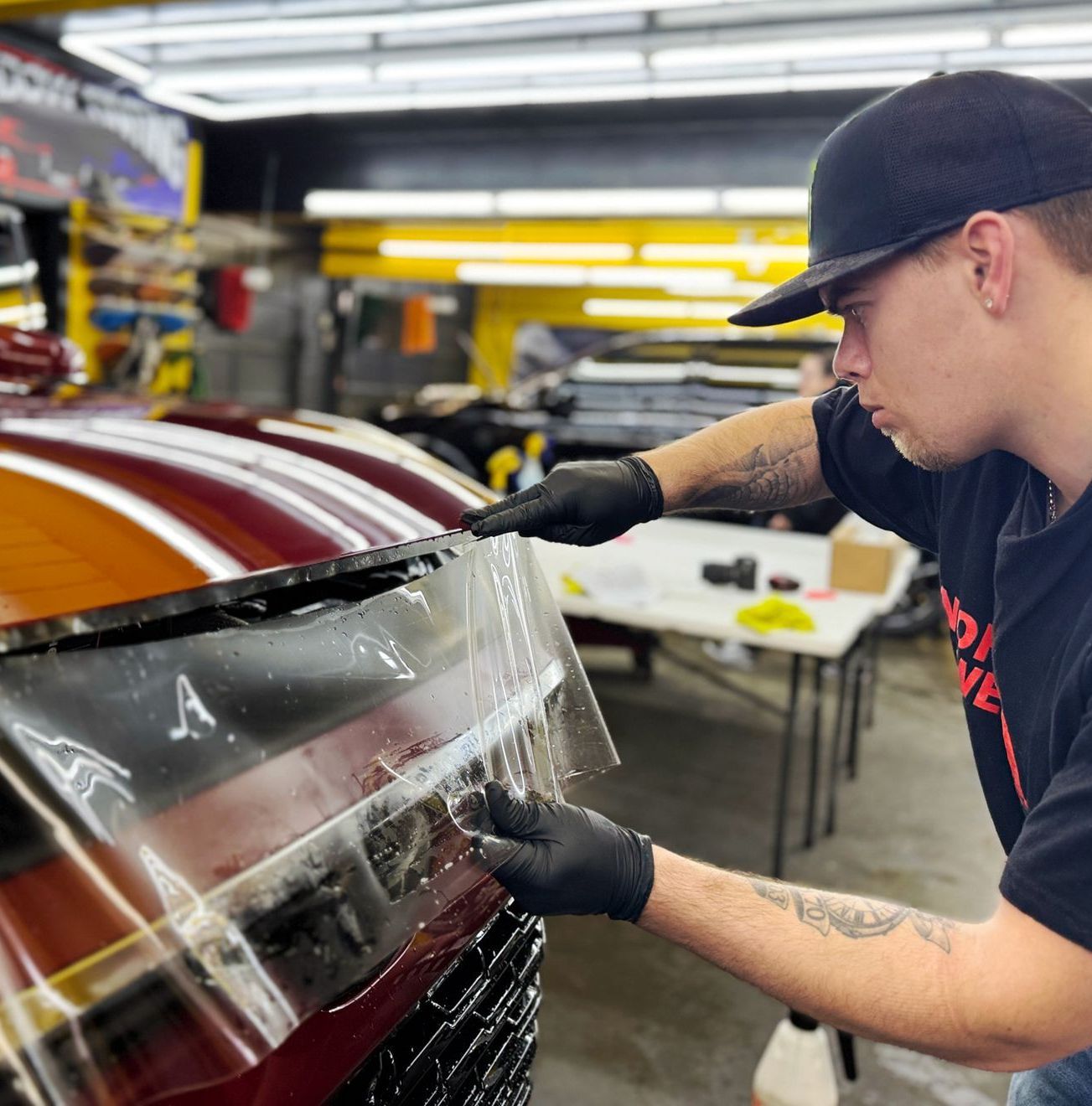 A person wearing black gloves is cleaning a white car with a cloth