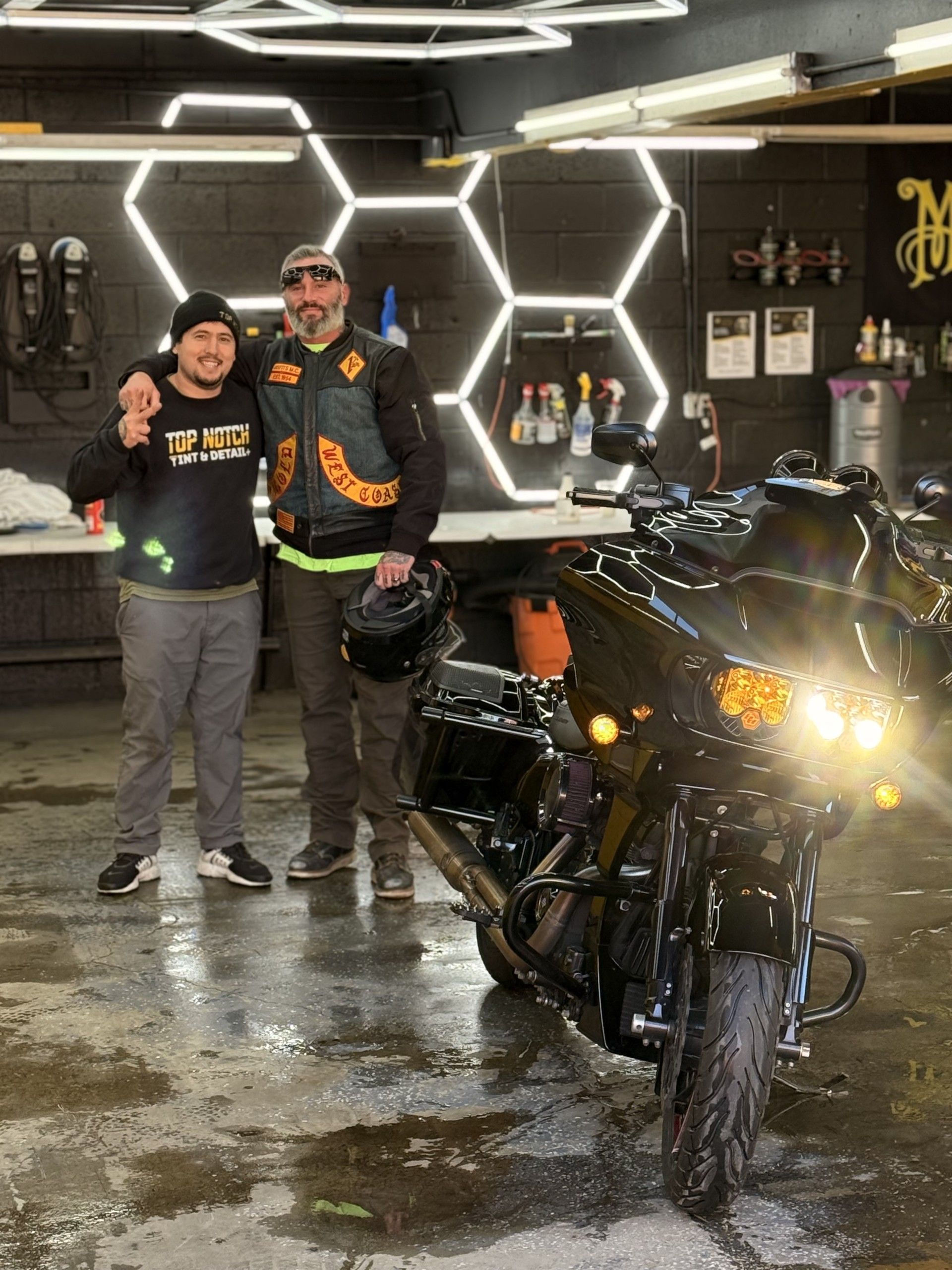 Two men are standing next to a motorcycle in a garage.