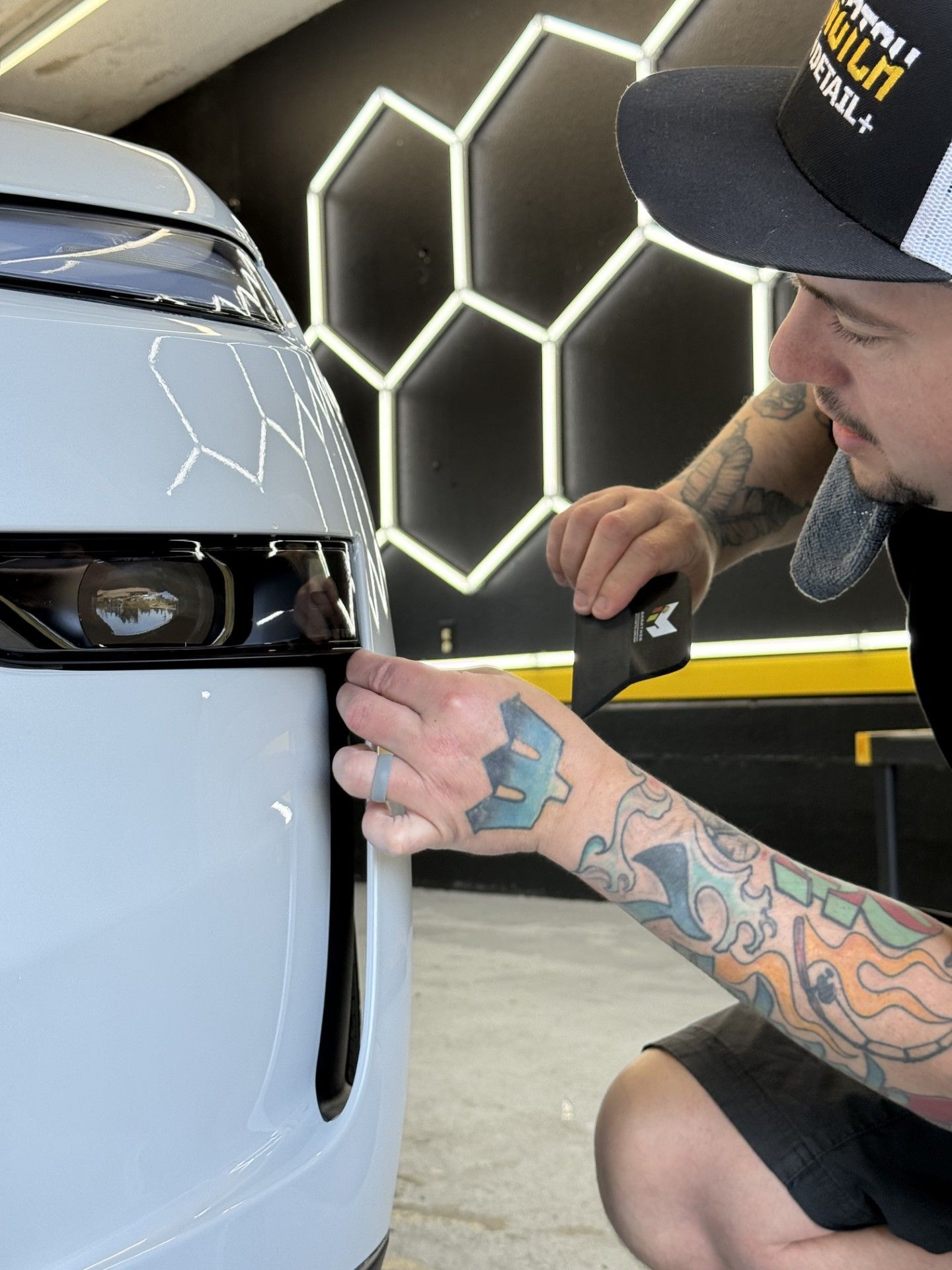 A man with a tattoo on his arm is installing PPF on a white car