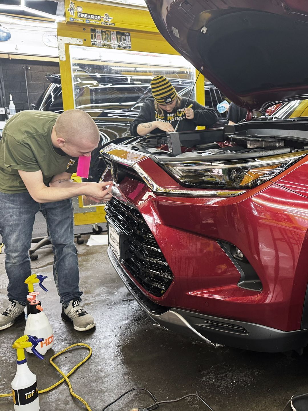 Two men are working on a red car in a garage.