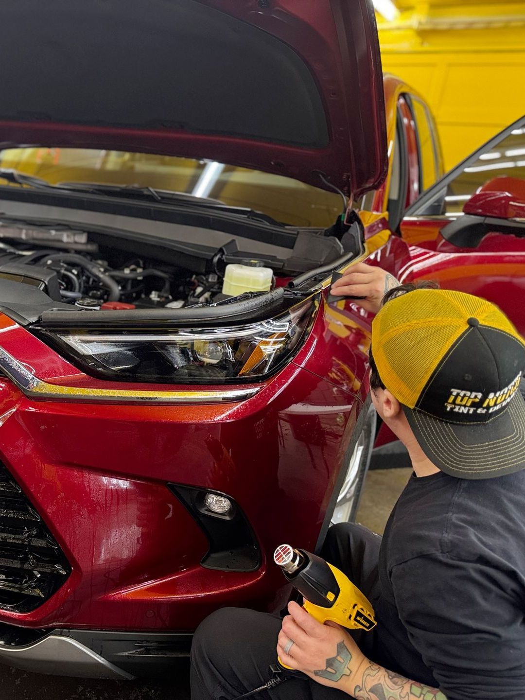 A man is working on the front of a red car.