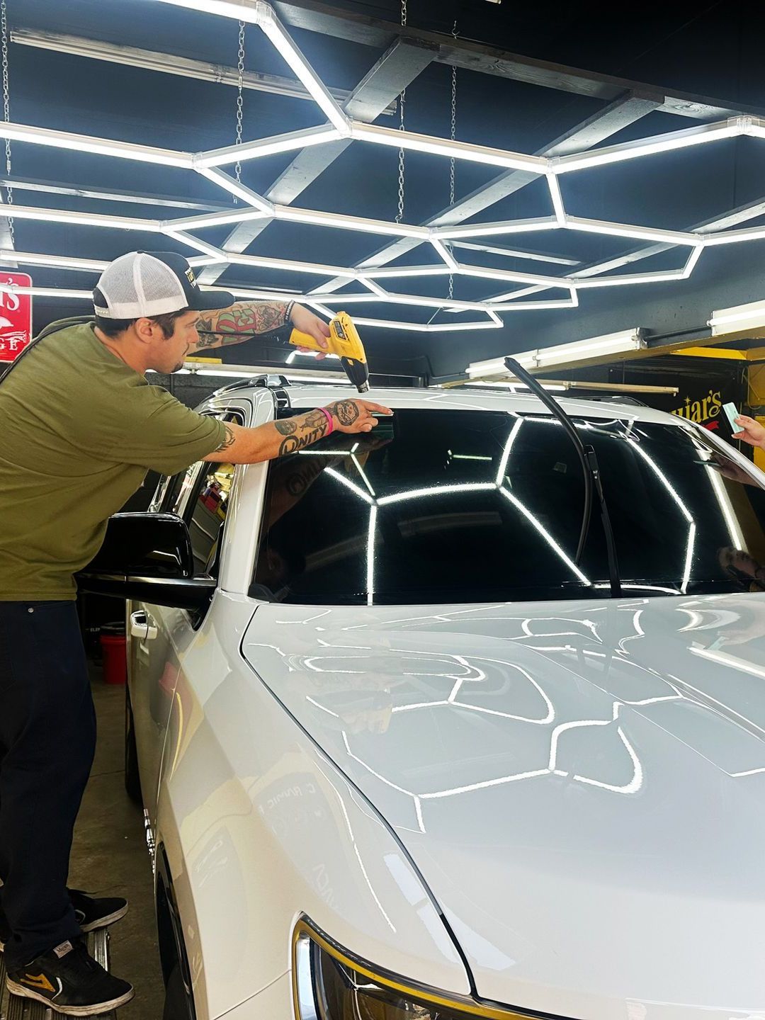 A man is cleaning the windshield of a white car in a garage.