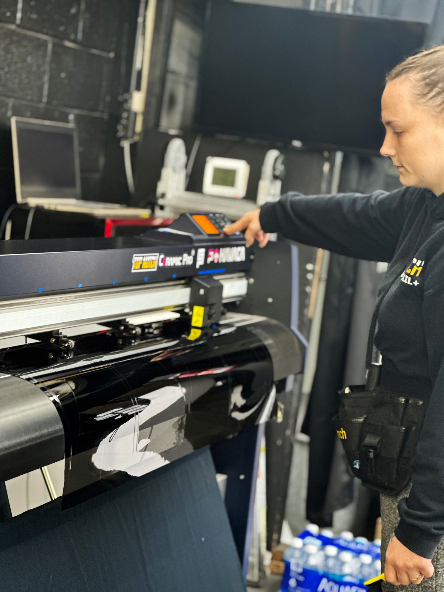 A woman is standing in front of a large printer.