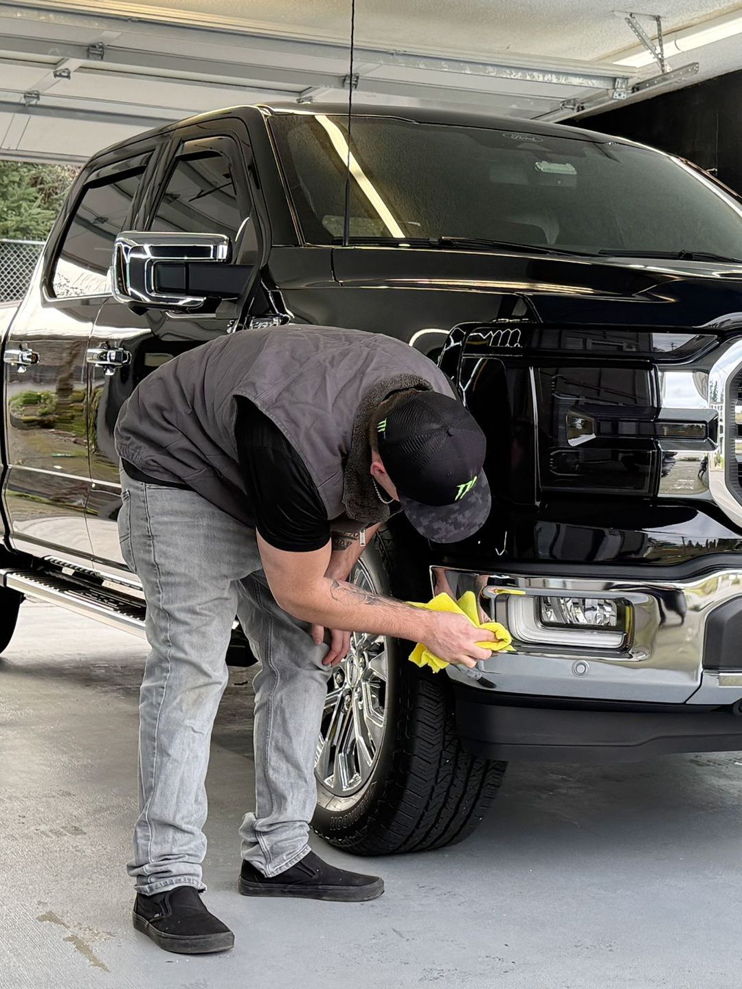 A man is cleaning the front bumper of a black truck.