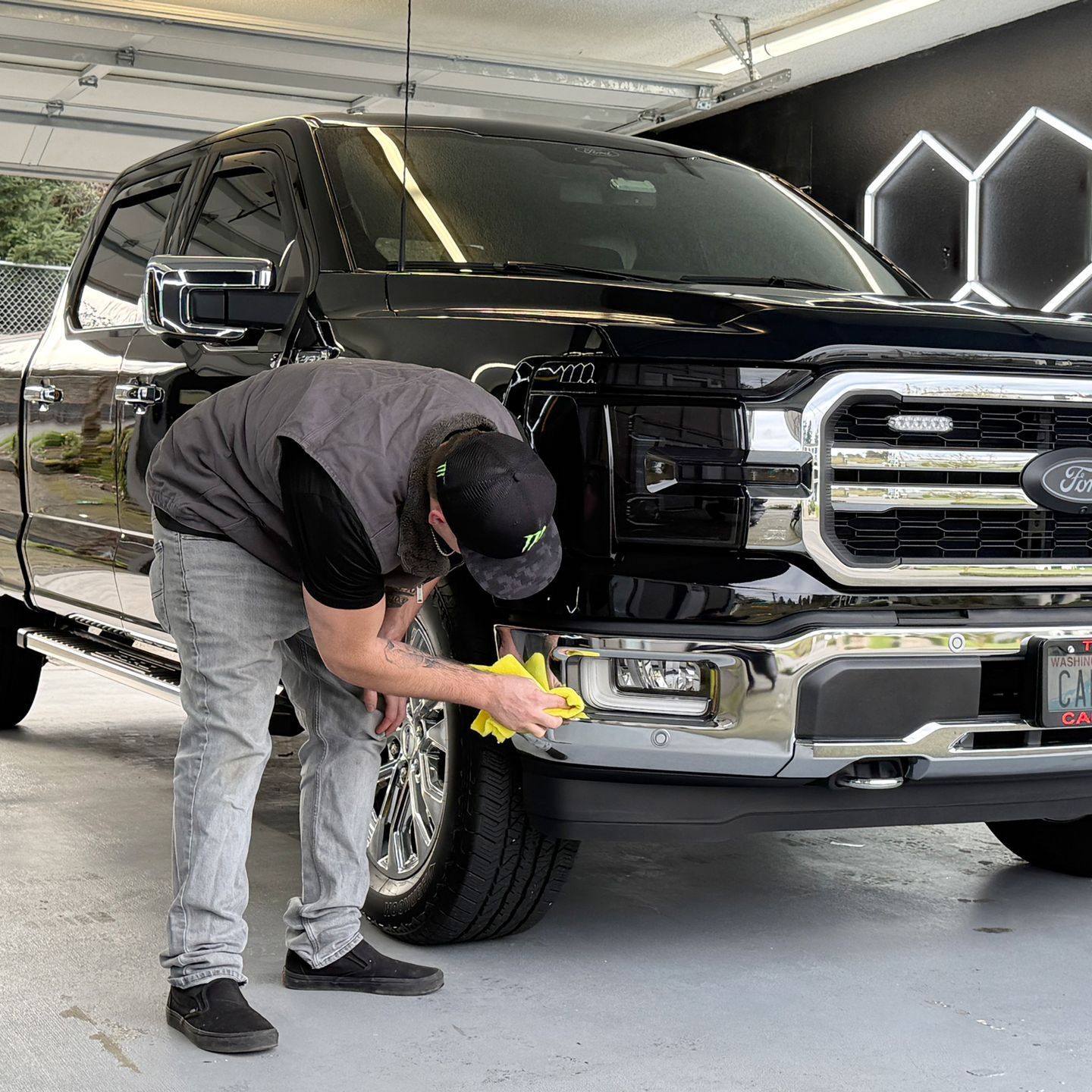 A man is cleaning the front bumper of a black truck.