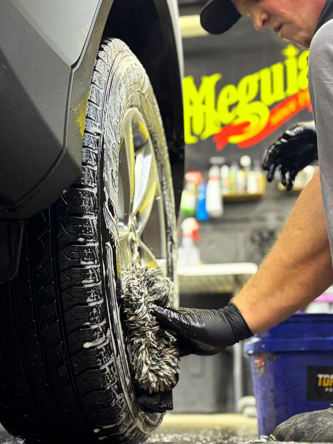 A man is cleaning a tire in front of a meguiar 's sign