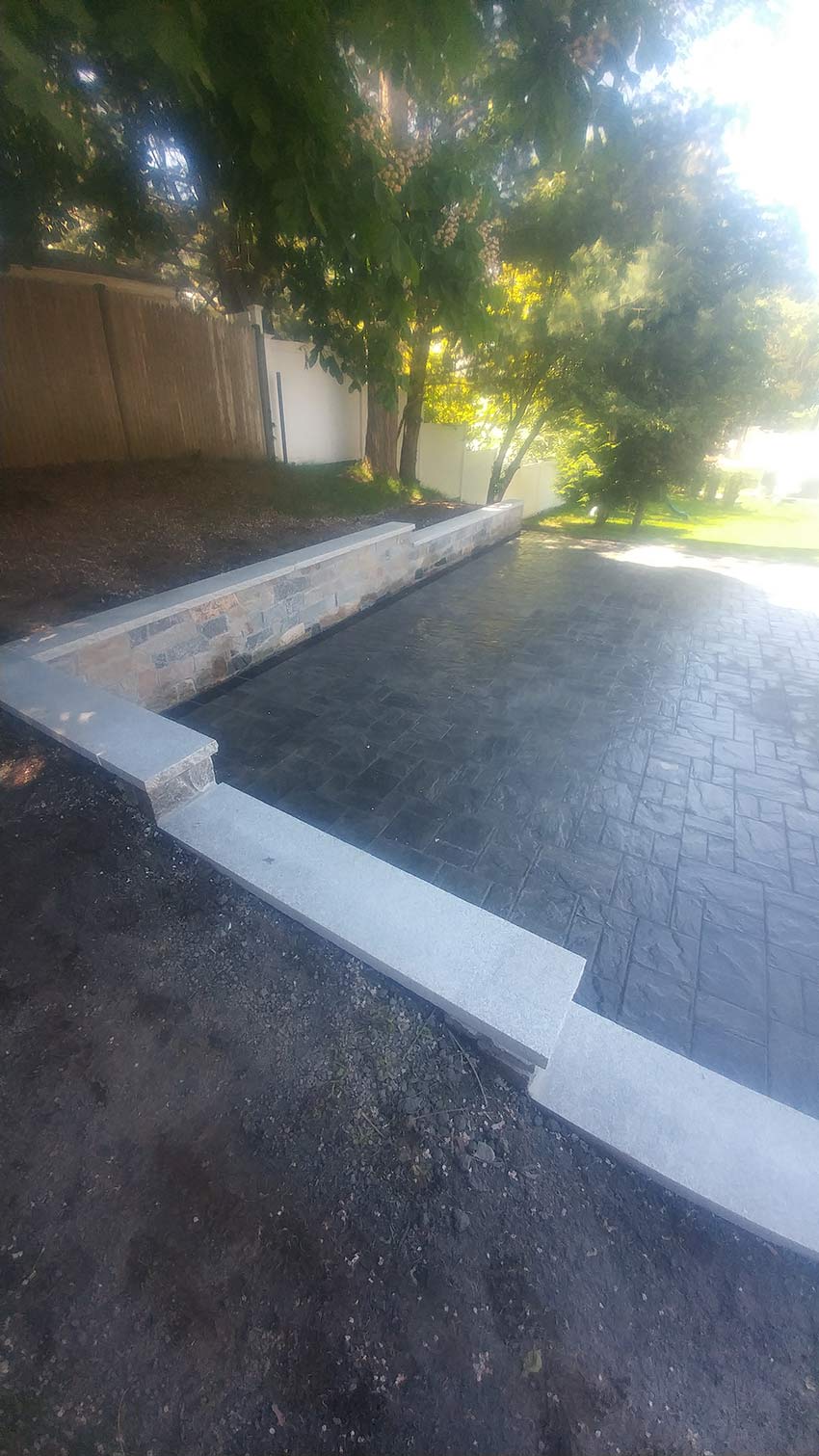 A concrete driveway with a stone wall and trees in the background.