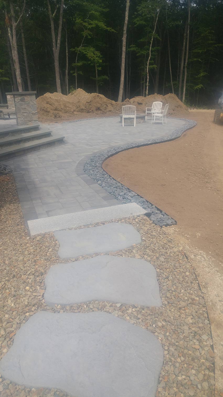 A walkway leading to a patio with chairs in the background.