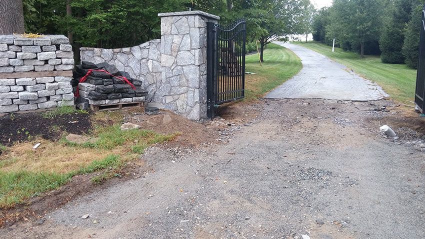 A gravel road with a stone wall and a gate