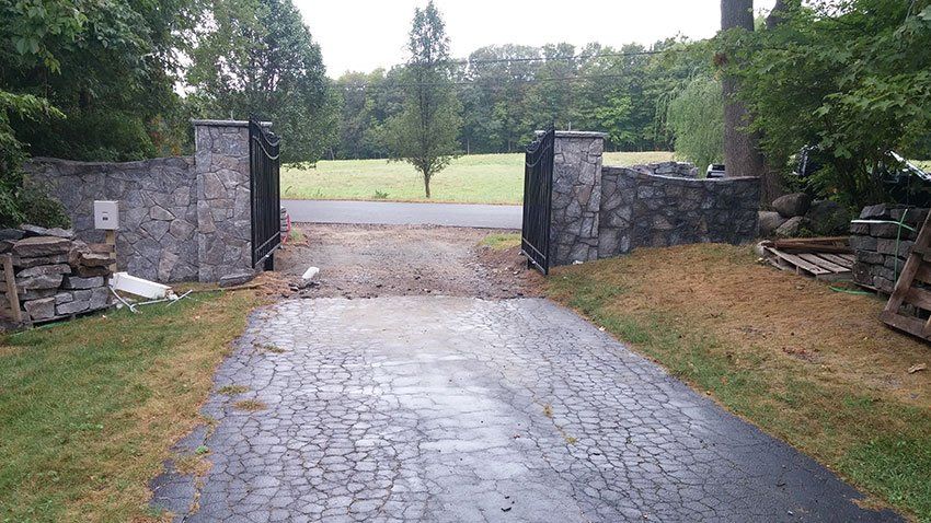 A driveway with a stone wall and a gate leading to a field.