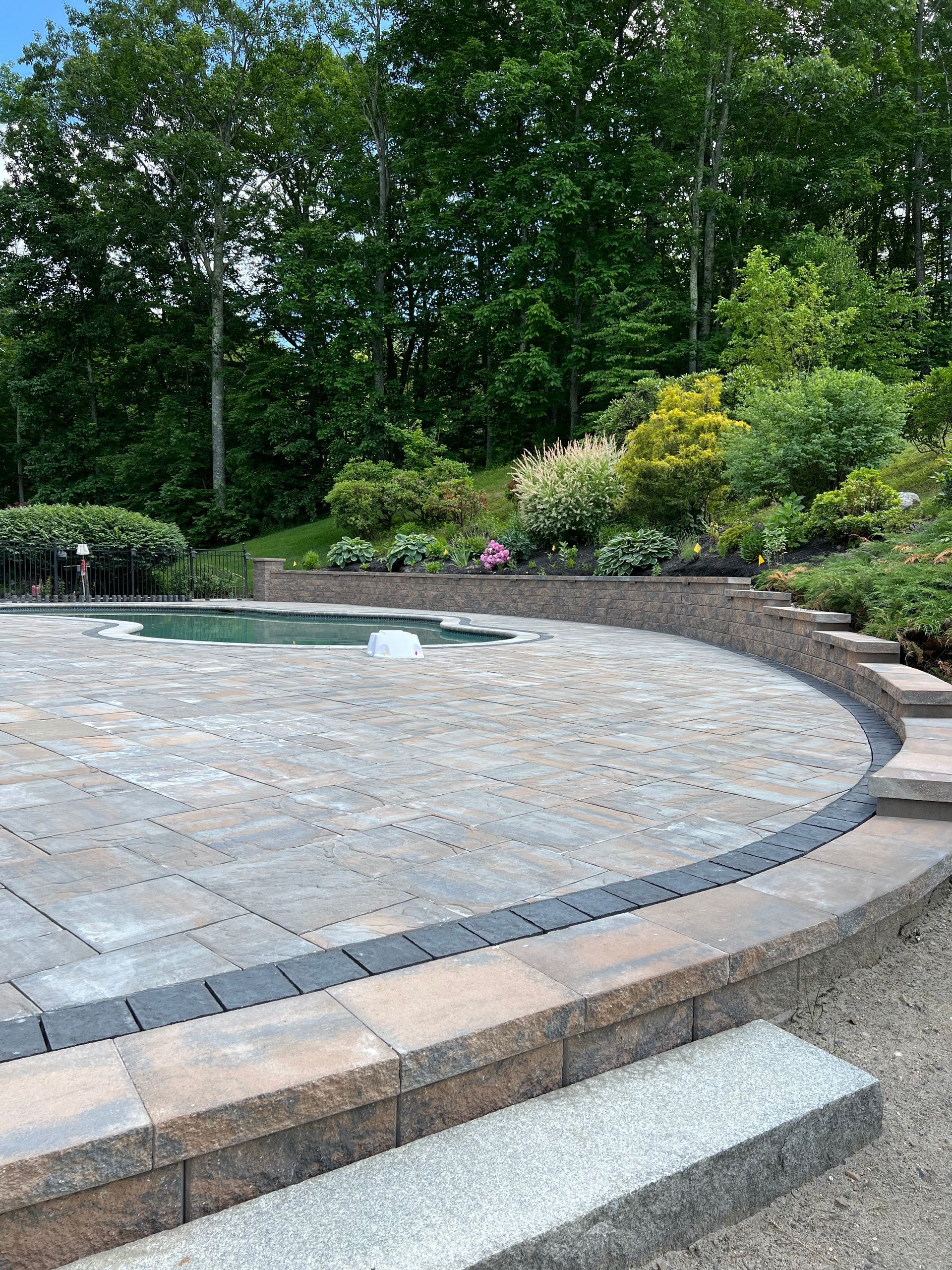 A patio with a pool in the background and trees in the background.
