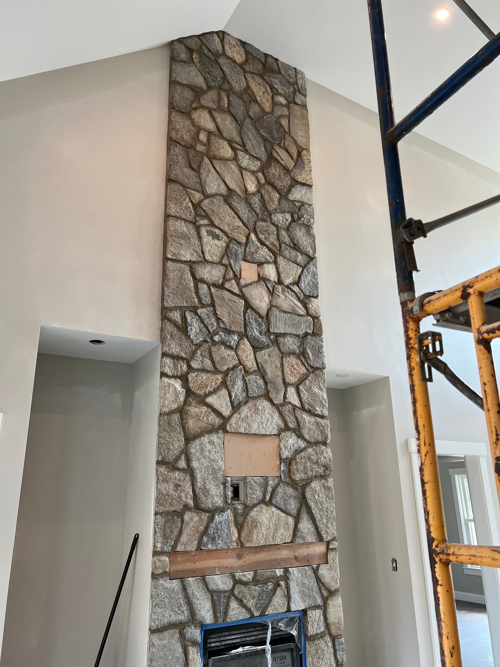 A stone fireplace in a living room with a scaffolding in the background.