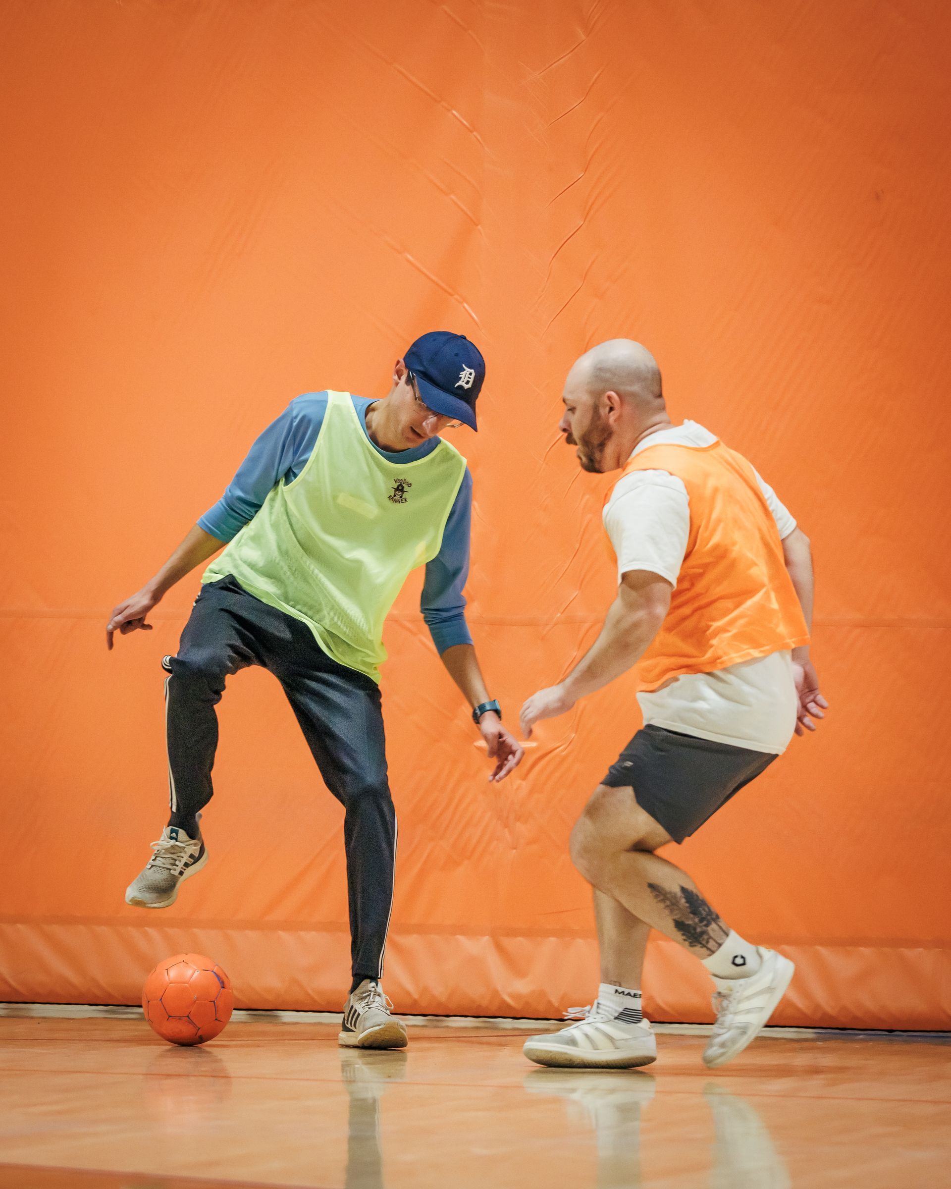 Two men compete for the soccer ball on a basketball court. 