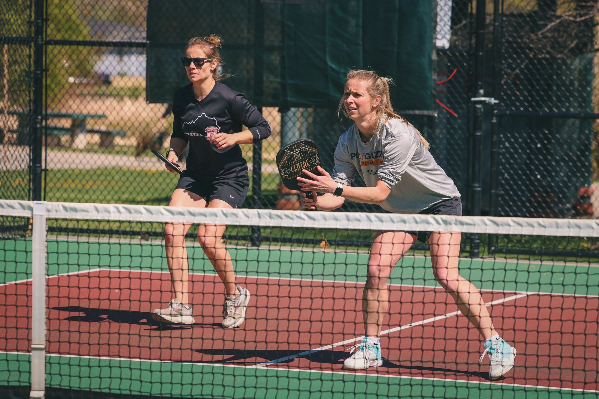 Two female pickleball players wait to return the serve.