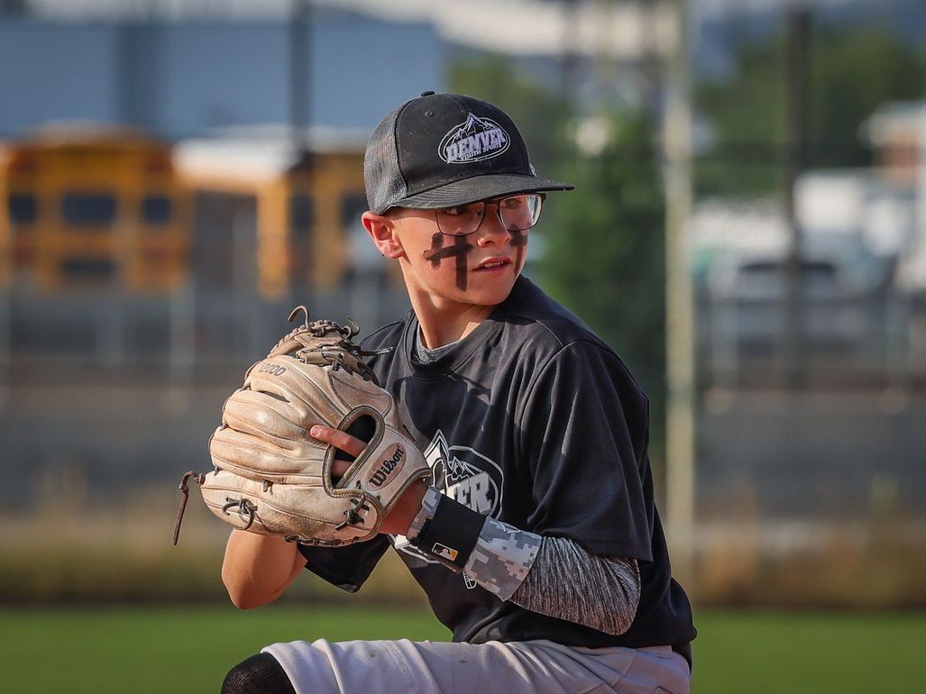 Youth baseball player winding up to throw a pitch wearing a Denver Parks and Recreation uniform.